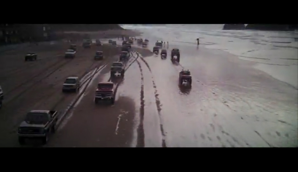 Screenshot of the car racing / truck rally opening sequence in The Goonies filmed by Haystack Rock on Cannon Beach.