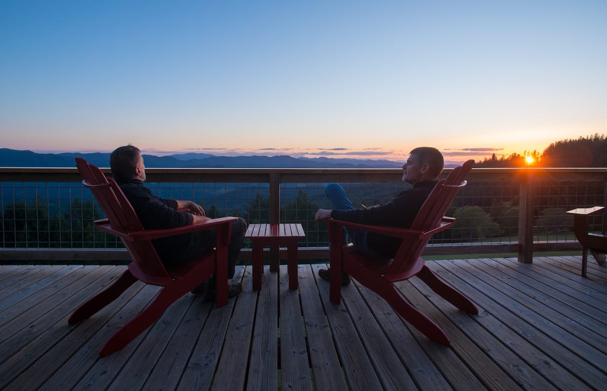 Two people sitting on the deck enjoying a sunset.