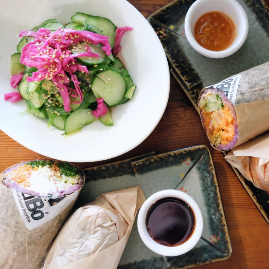 sushi burritos arranged on a table with cucumber salad and sauces