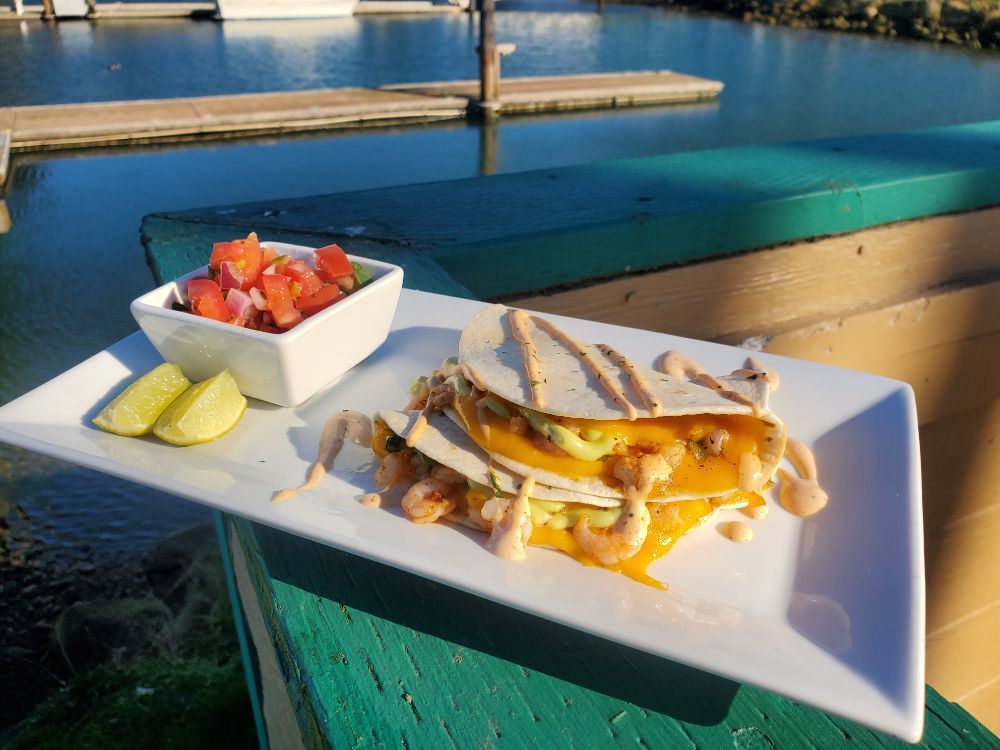 Two quesadillas sitting on a green deck railing looking out to the bay.