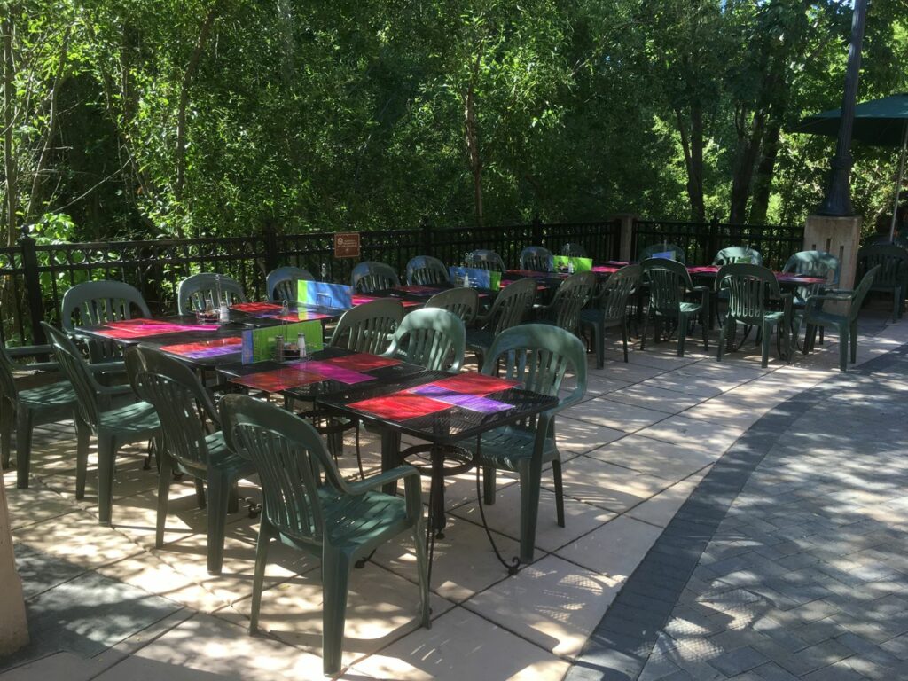 A shaded patio with outdoor seating and green trees at Louie's.