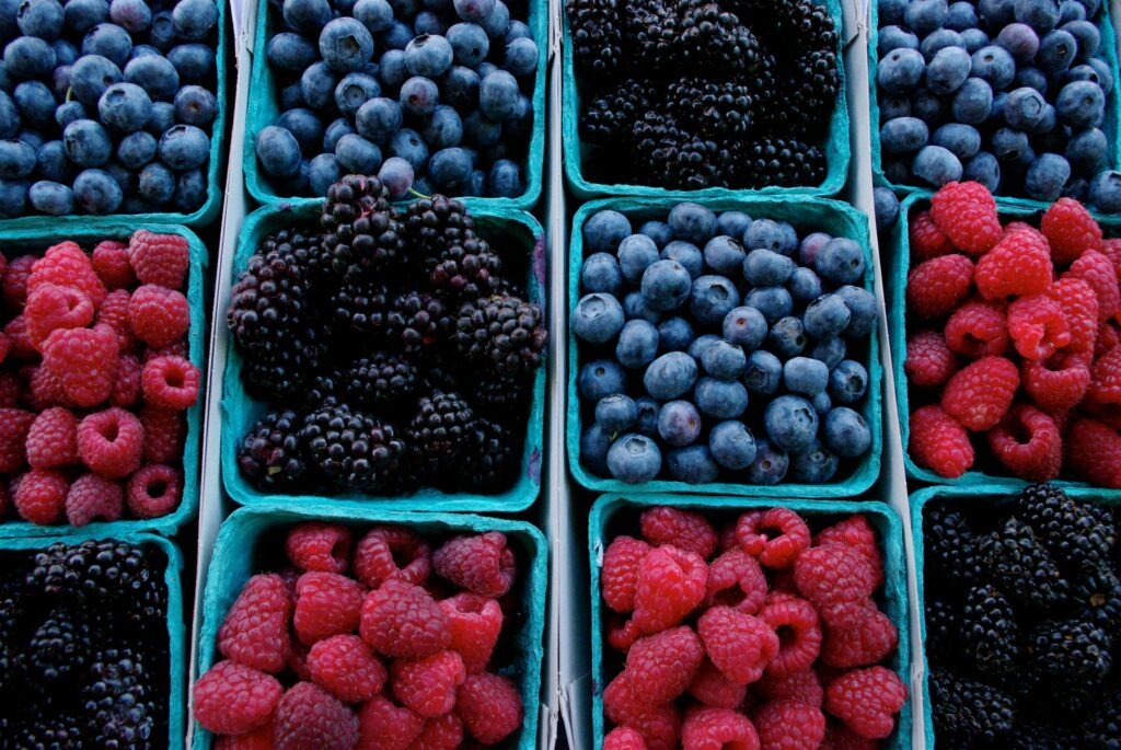 Green containers of berries including raspberries, blackberries, and blueberries.