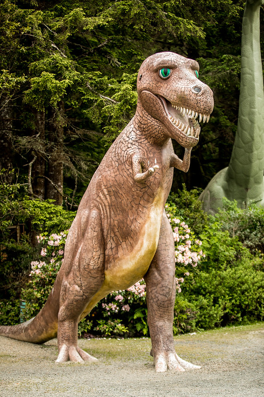A tall brown dinosaur sculpture with green eyes and sharp teeth at the Prehistoric Gardens.