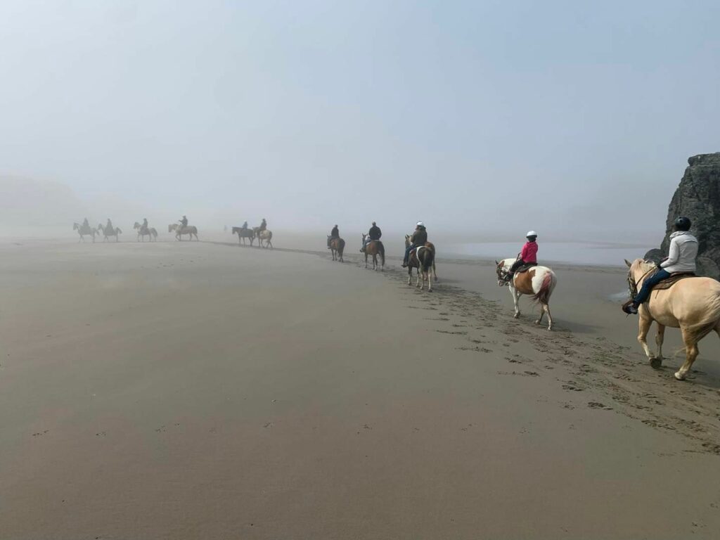 A group of people rides horses down the beach in the fog in Bandon, Oregon.
