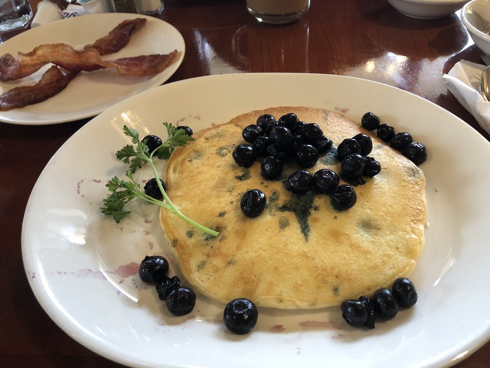 Delicious looking blueberry pancakes topped with fresh blueberries on a white plate.