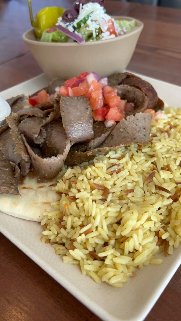 Sliced meat, pita bread, rice, and a bowl with a Greek salad.