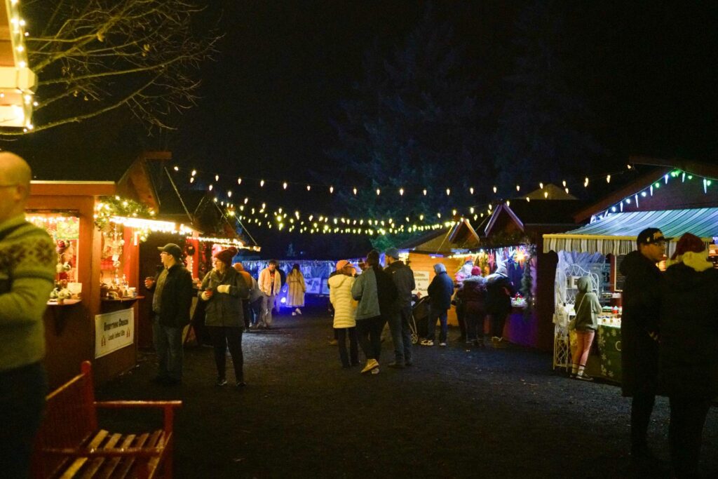 Food and craft booths at the Silverton Christmas Market.  Warm white lights are strung overhead across the path.