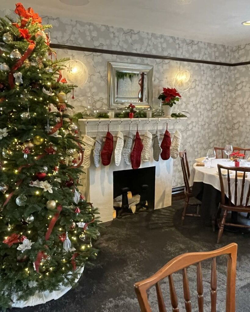 The Joel Palmer House Restaurant dining room decorated for Christmas. There's a Christmas tree and stockings hung on the mantle above a fireplace.