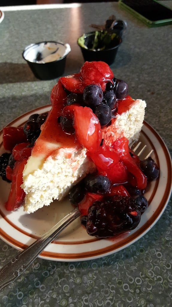 A delicious looking piece of cheesecake topped with a variety of red and blue berries.