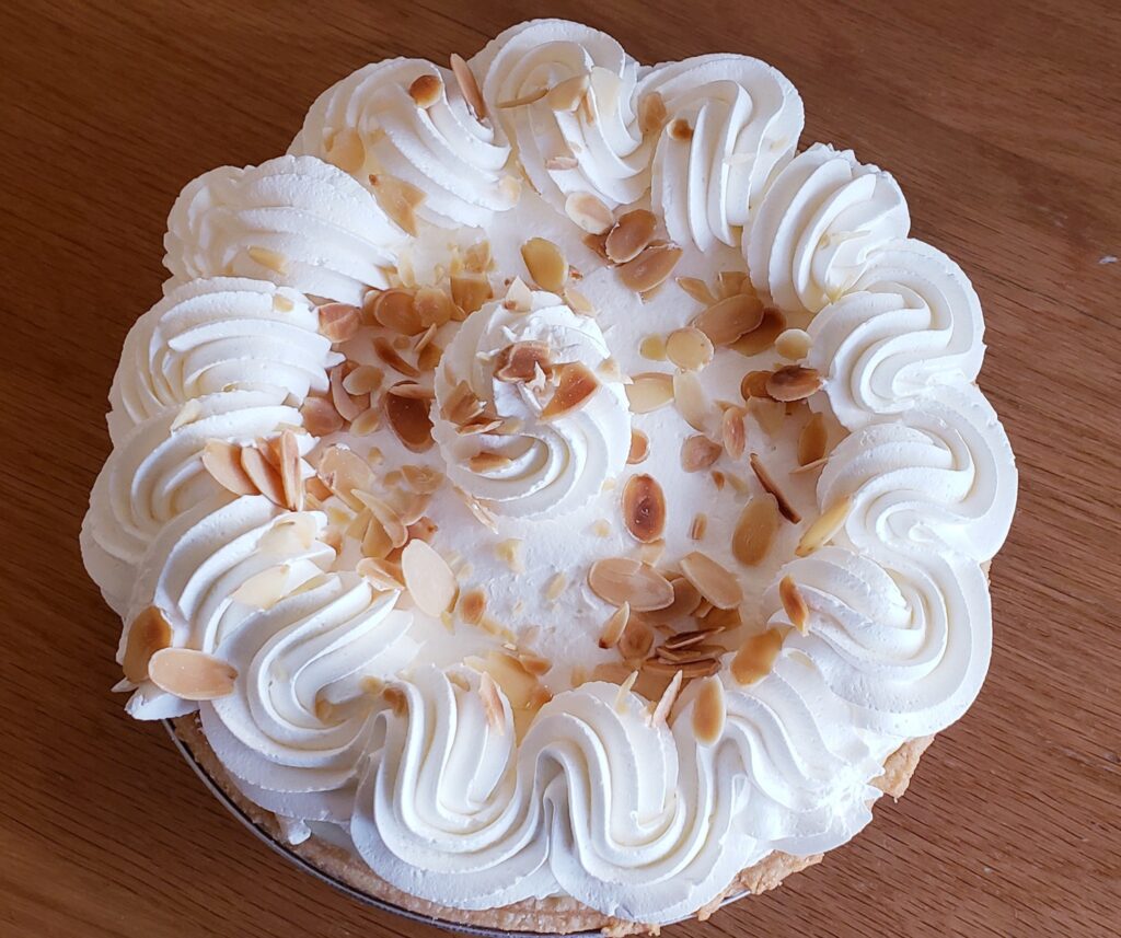 A whole pie with white whip or frosting on top and sliced nuts sprinkled on top.