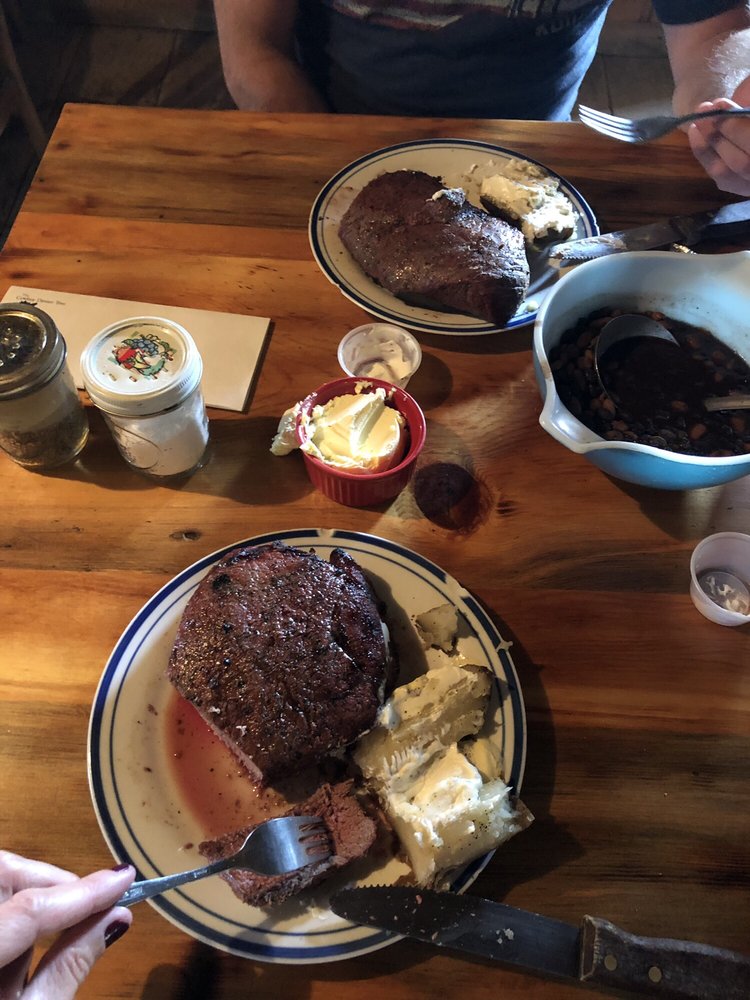 Steak, potatoes and cowboy beans on a wooden table at the Cowboy Dinner Tree.