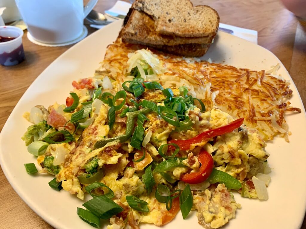 A plate with toast, hash browns, and scrambled eggs with various red and green vegetables. Looks tasty!