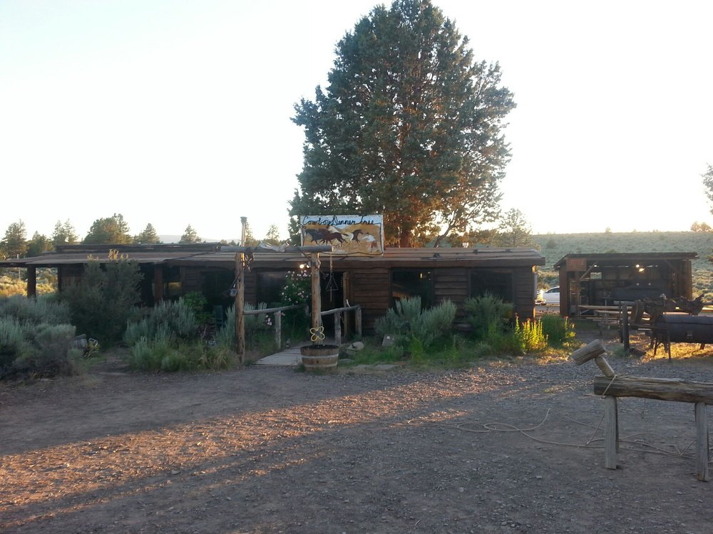 The outside of The Cowboy Dinner Tree. It's a rustic wood building with sage brush outside and saddles hanging over a wooden rail.