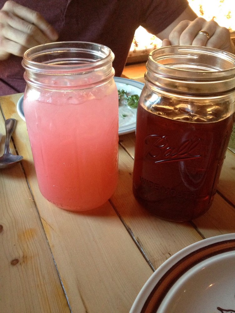 Two glass mason jars. One is full of pink lemonade, the other has tea.