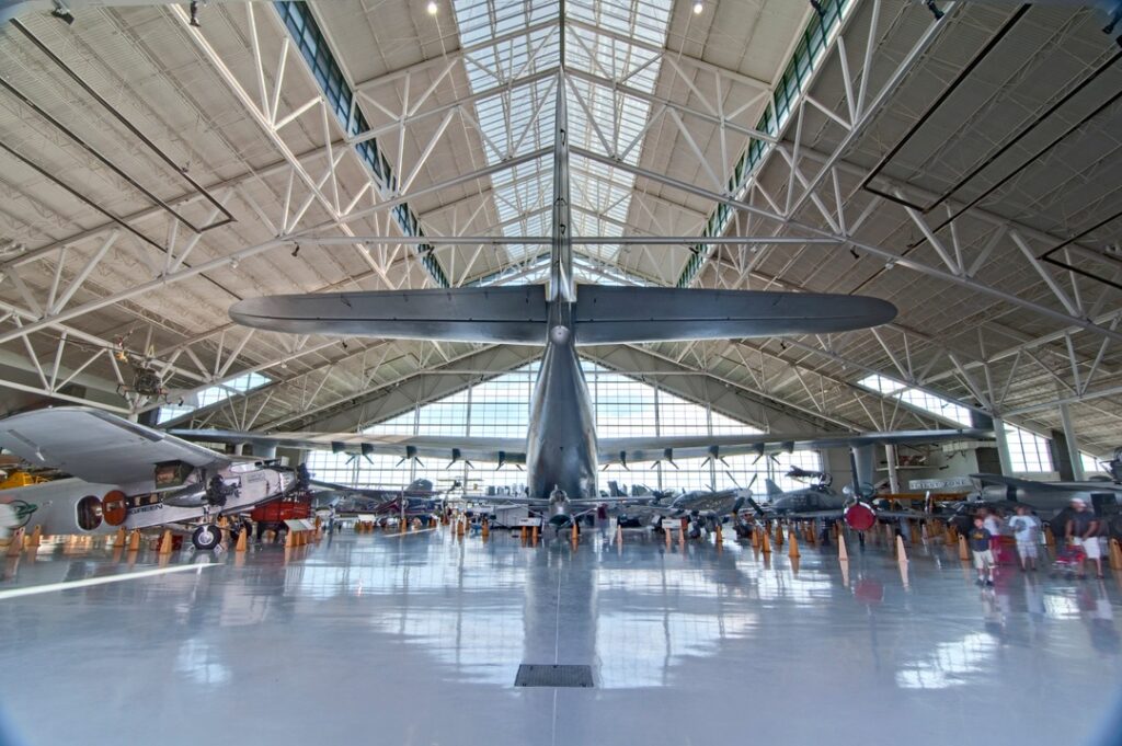 The Spruce Goose inside the Evergreen Aviation And Space Museum.  It takes up a huge amount of space in the main museum area.  It sits in front of large windows, casting the massive plane in daylight.